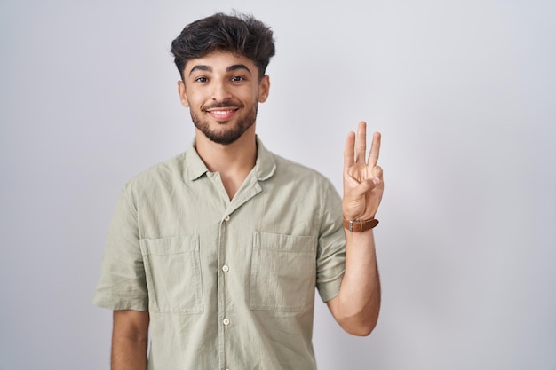 Arab man with beard standing over white background showing and pointing up with fingers number three while smiling confident and happy