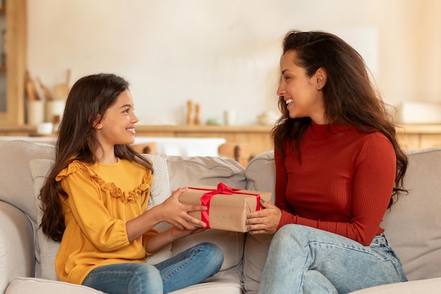 Arab mom giving wrapped present box to daughter at home