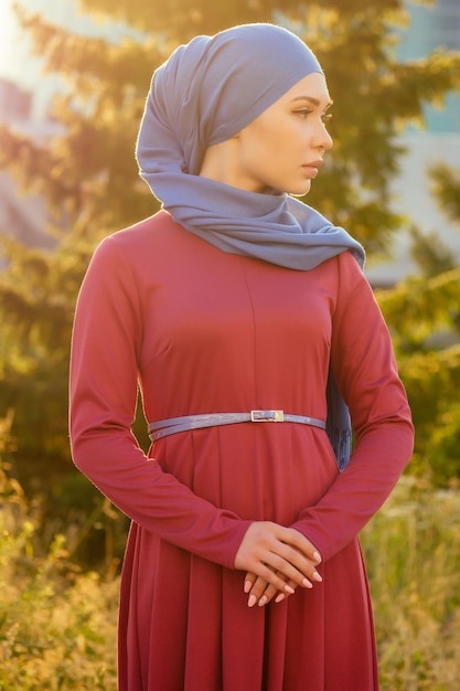 夏の公園を背景に通りに立っている化粧をしたアラブのイスラム教徒のビジネス女性ヒジャーブ。女性はスタイリッシュなアバヤとショールを着ています