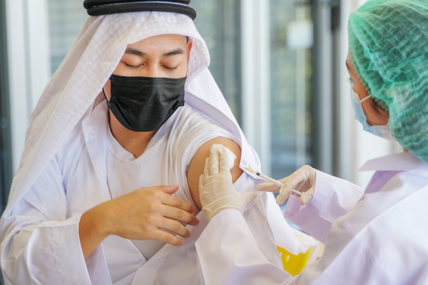 Arab Muslim man sitting to get covid vaccine in hospital with hand nurse injecting vaccine