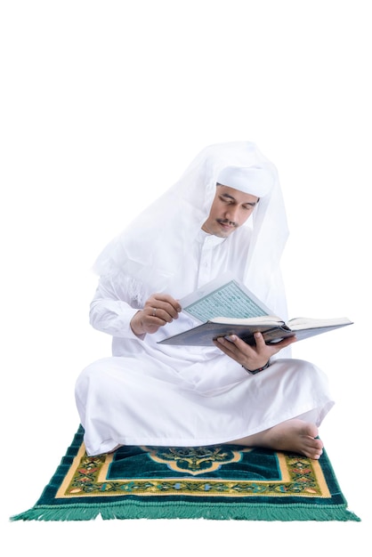 Arab Muslim man sitting and reading the Quran on the prayer rug