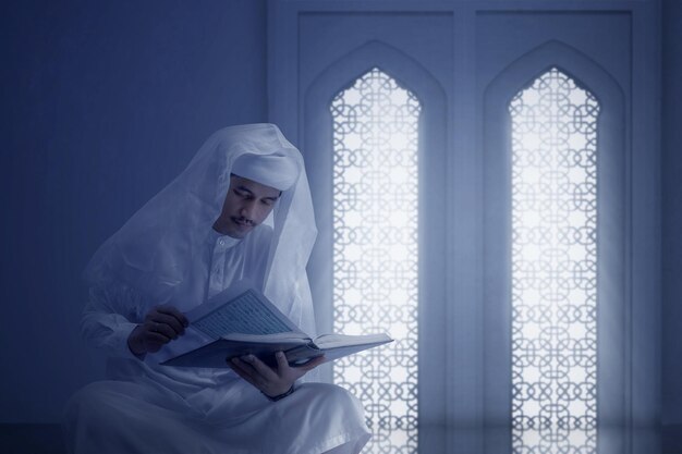 Uomo arabo musulmano seduto e leggendo il corano