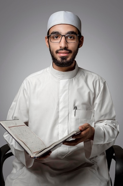 An Arab Muslim young man wearing an Islamic galabiya and holding the Qur'an in his hand