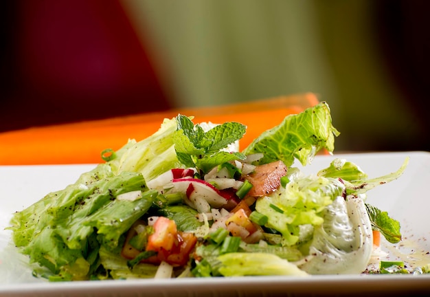 Арабский салат с оранжевой тканью и белой тарелкой, помидорами, луком, зеленым луком, петрушкой, редисом, мятой, оливками, курицей.