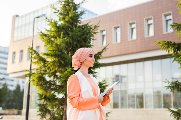 Arab Student holding a folder. Young beautiful Muslim woman walk in the city.