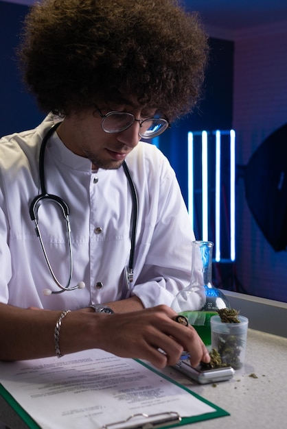 Арабский студент с афро-прической в костюме врача занимается исследованием каннабиса