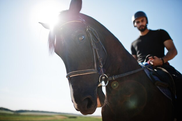 아랍의 키가 큰 수염 남자는 검은 헬멧을 쓰고 아라비아 말을 탄다.