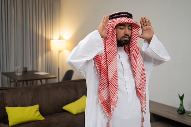 An arab in a turban prays during the takbir movement with two hands