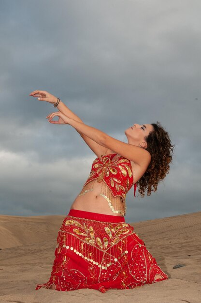 Arab woman dancing belly dance in the desert dunes at sunset