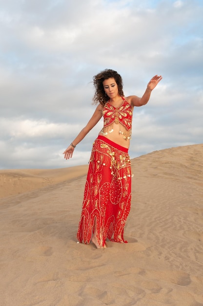 Arab woman dancing belly dance in the desert dunes at sunset