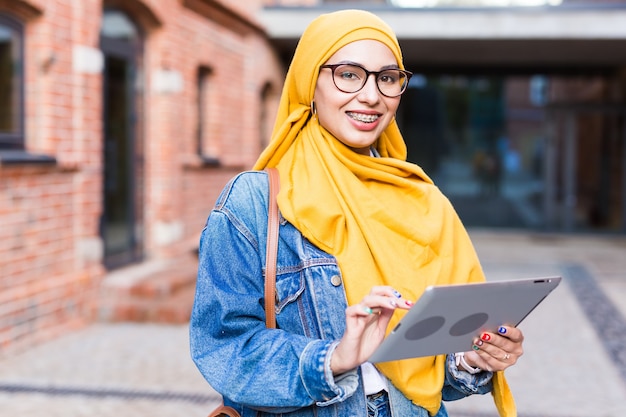 Arab woman student. Beautiful muslim female student wearing bright yellow hijab holding tablet.