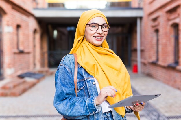 아랍 여자 학생. 밝은 노란색 hijab 지주 태블릿을 입고 아름 다운 이슬람 여성 학생.