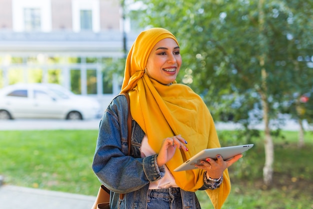 아랍 여자 학생. 밝은 노란색 hijab 지주 태블릿을 입고 아름 다운 이슬람 여성 학생.