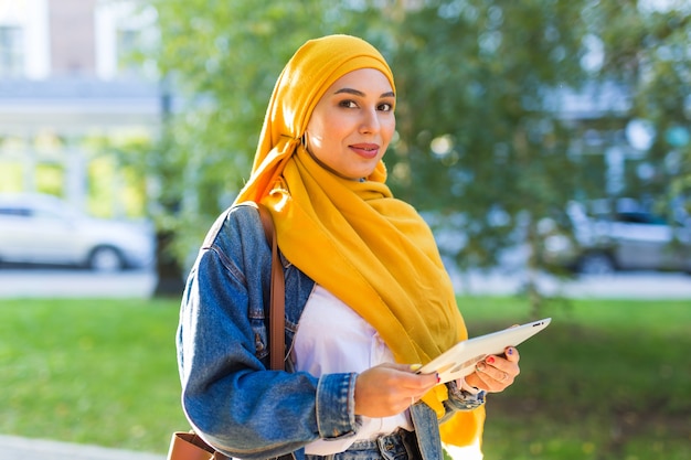 Photo arab woman student. beautiful muslim female student wearing bright yellow hijab holding tablet.