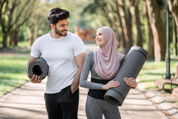 Arabian couple in sportswear standing at park with yoga mats