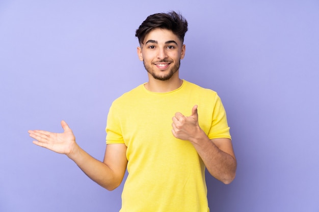 Arabian handsome man over isolated holding copy space imaginary on the palm to insert an ad and with thumbs up