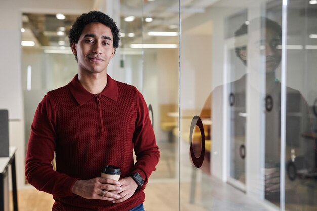 Arabian man holding coffee cup standing in office and looking at camera