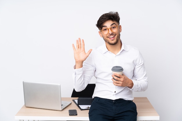 Arabian man in a office on white wall saluting with hand with happy expression