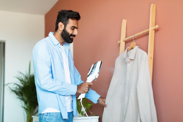 Arabian man steaming his clothing with steamer device at home