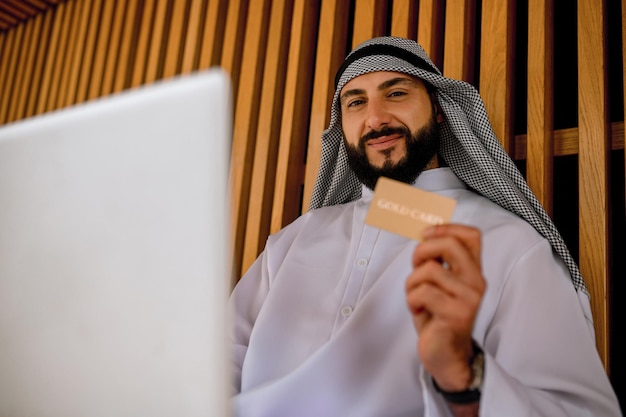 An arabian man in traditional clothing holding a credit card