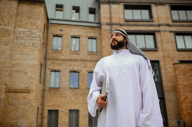 Un uomo arabo in abiti tradizionali con un laptop in strada