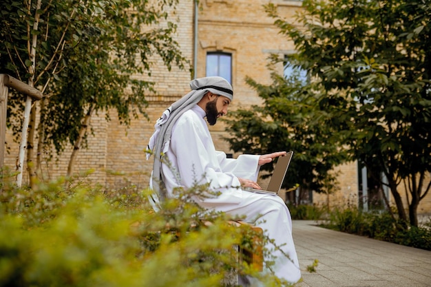 An arabian man in traditional clothing with a laptop in the street