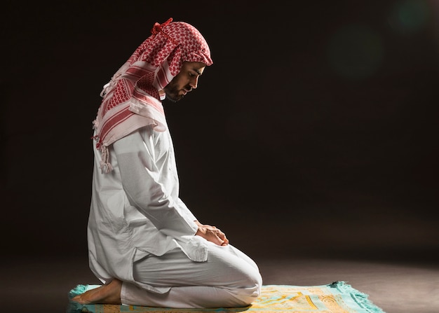 Arabian man with kandora sitting on prayer rug side view