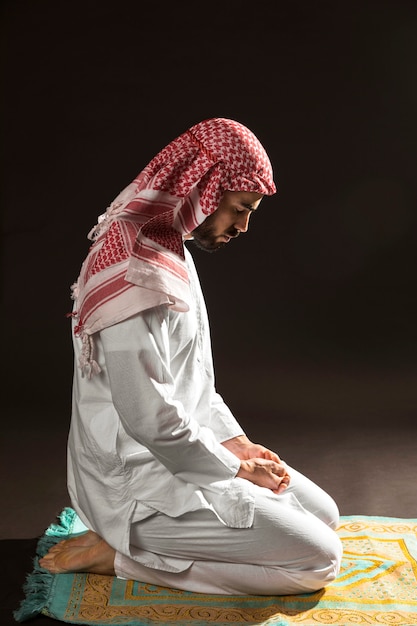 Arabian man with kandora sitting on prayer rug sideways