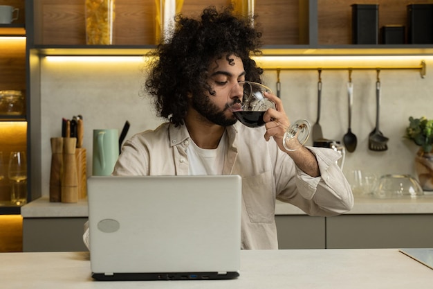 L'uomo arabo lavora online sul laptop godendosi un bicchiere di vino