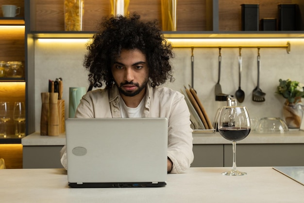 アラビア人はワインのグラスを楽しんでラップトップでオンラインで動作します