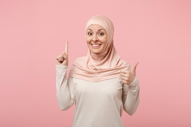히잡 가벼운 옷을 입은 아라비아 이슬람 여성이 분홍색 배경에 고립되어 포즈를 취하고 있습니다. 사람들이 종교 이슬람 생활 방식 개념입니다. 복사 공간을 비웃습니다. 엄지손가락을 보여주는 좋은 아이디어로 검지 손가락을 들고.