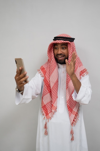 An arabian youth in a turban makes a video call using a mobile phone while smiling with a hand gesture