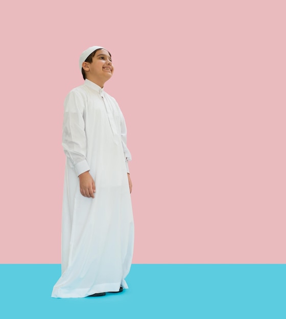 写真 青とピンクの背景に伝統的な服を着たアラブの少年が微笑んでいる