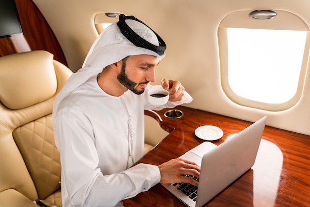 Arabic businessman with traditional dress flies in exclusive business class on airplane 