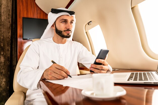 Arabic businessman with traditional dress flies in exclusive business class on airplane 