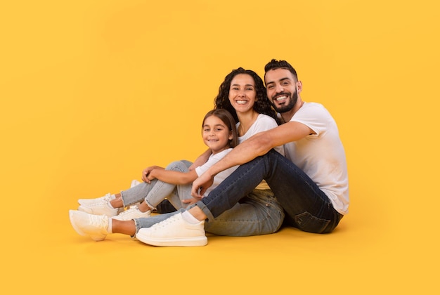 Arabic father mother and daughter hugging sitting over yellow background