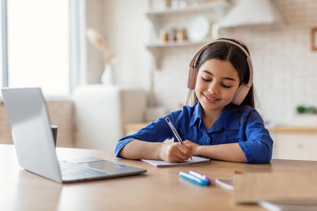 Arabic girl in headphones studying with laptop taking notes indoor