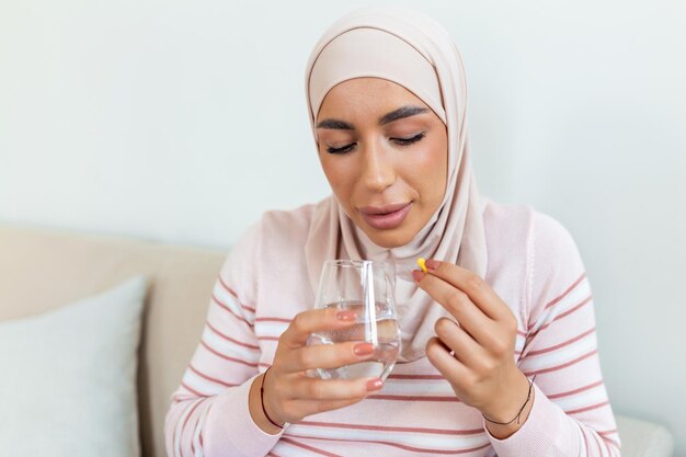 Arabic ill sick muslim woman taking painkiller medicine to relieve stomachache pain sit on bed in th