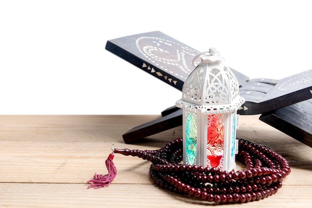 Арабская лампа с разноцветным светом и четками на деревянном столе с белым фоном