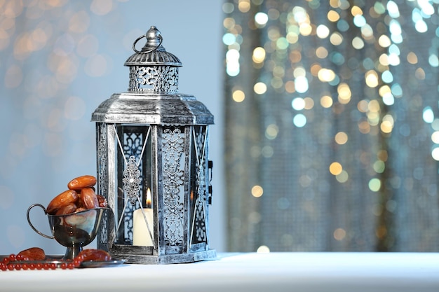 arabic lantern misbaha and dates on table against blurred lights space for text
