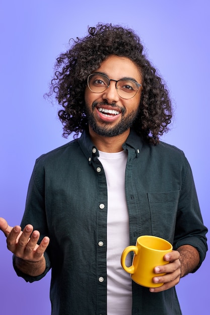 Uomo arabo che guarda, beve il tè e parla, sorridendo. isolato su muro viola