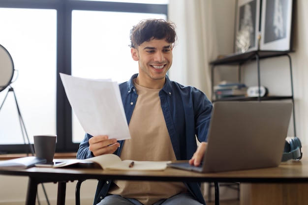 Arabic man using laptop holding papers sitting at desk indoors