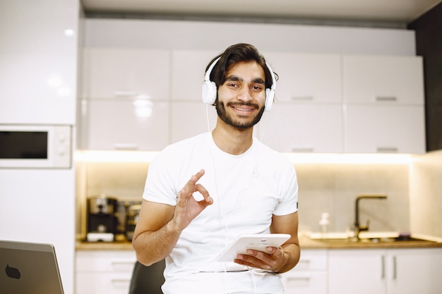 Uomo arabo che guarda un webinar online, seduto in cucina con un tablet che si gode l'apprendimento a distanza
