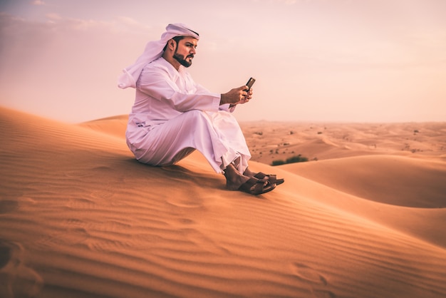 Arabic man with traditional emirates clothes walking in the desert