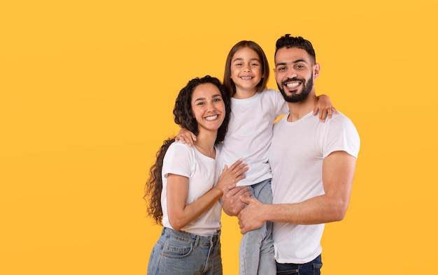 Photo arabic parents and daughter embracing together posing on yellow background