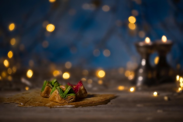 Arabic sweets on a wooden surface Candle holders night light and night blue sky with crescent moon in the background