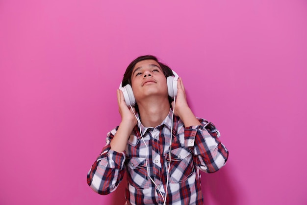 ヘッドフォンを着用し、音楽を聞いているアラビア語の10代の少年ピンクの背景