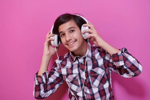 ヘッドフォンを着用し、音楽を聞いているアラビア語の10代の少年ピンクの背景