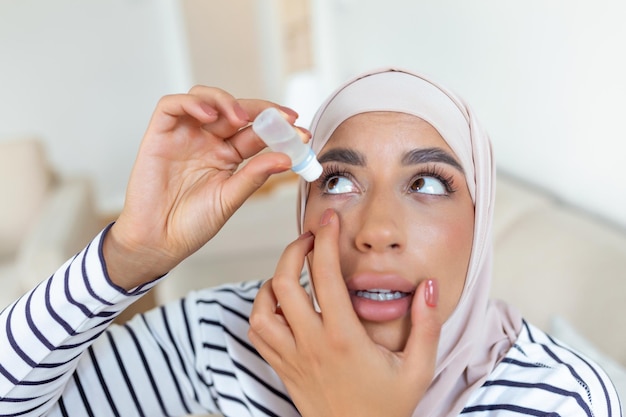 Arabic woman with hijab using eye drop dropping eye lubricant to treat dry eye or allergy sick woman treating eyeball irritation or inflammation woman suffering from irritated eye optical symptoms