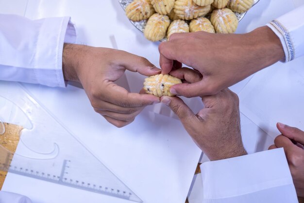 Arabic working colleagues hands eating eid kahk together on working desk